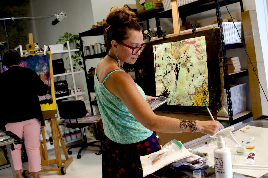 Smiling artist holding palette beside her painting in the studio
