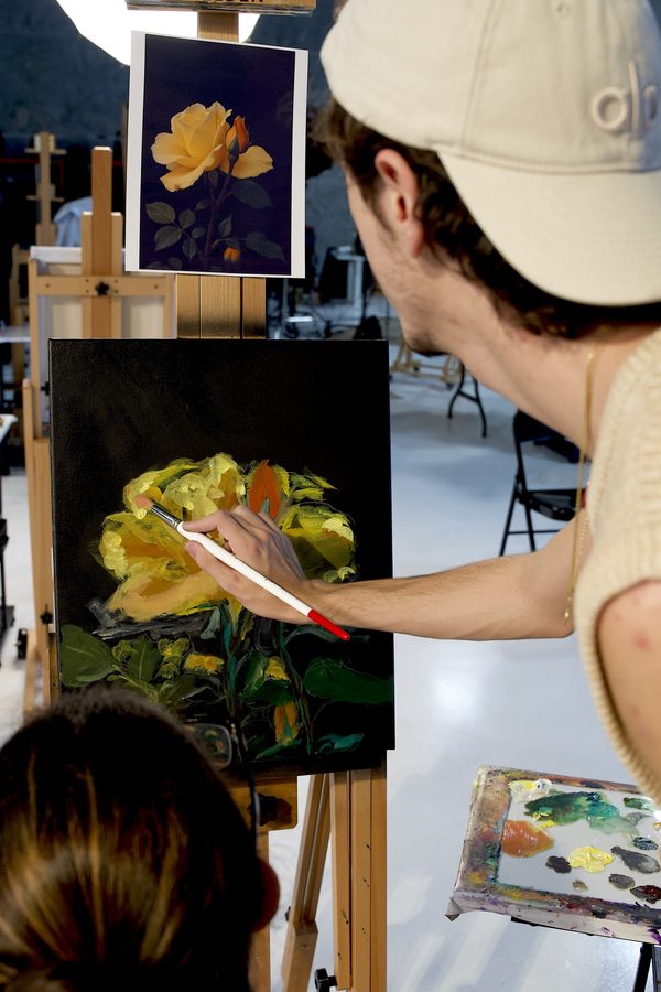 Instructor guiding a student painting a floral canvas at the easel