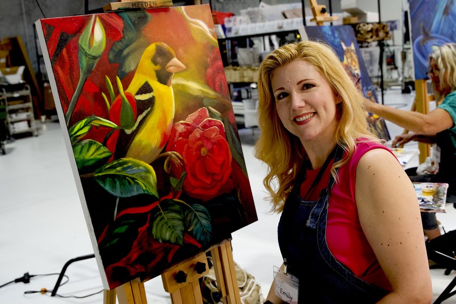 Smiling artist beside her bold red floral painting on the easel