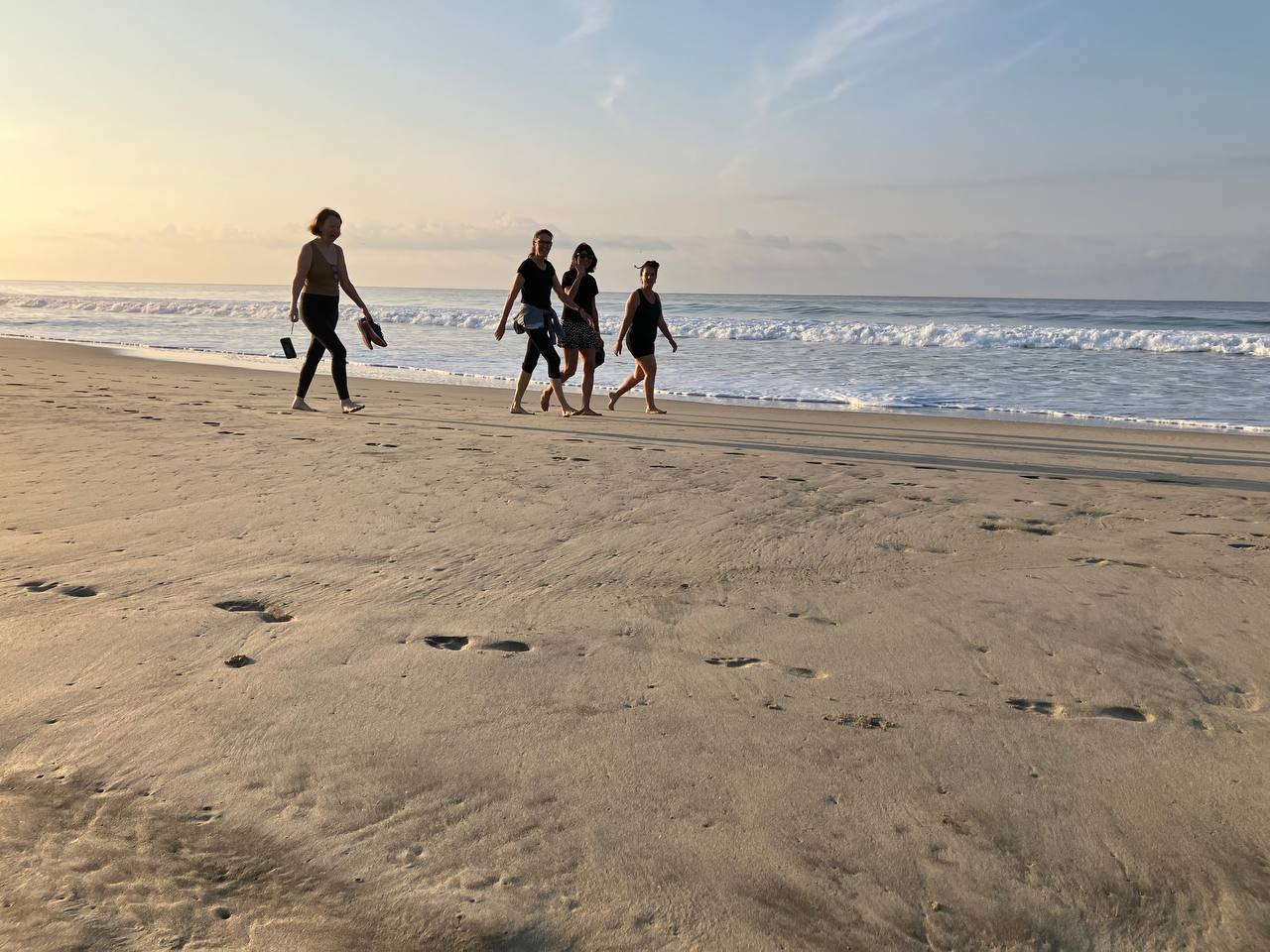 Four people walking along a wide empty beach at low sun, footprints across the sand in front of them and the surf breaking behind