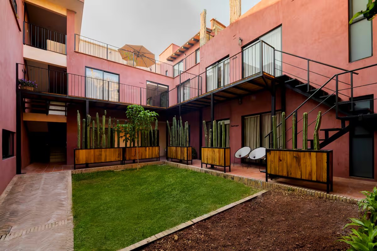 A terracotta-pink courtyard with cactus in wooden planters, a lawn, upper walkways and an external steel stair